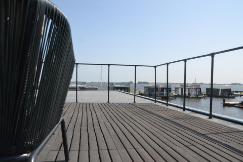 Große Terrasse mit Blick auf das Wasser und Hausboote bei Houseboat 'Riggelbrug' in Friesland, Niederlande.