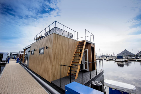 Casa flotante moderna 'Riggelbrug' en Welcome In - Friesland, Países Bajos, atracada en una marina tranquila.