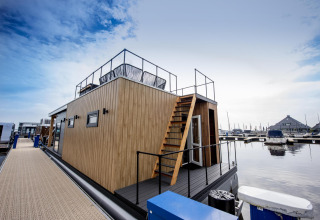 Casa flotante moderna 'Riggelbrug' en Welcome In - Friesland, Países Bajos, atracada en una marina tranquila.