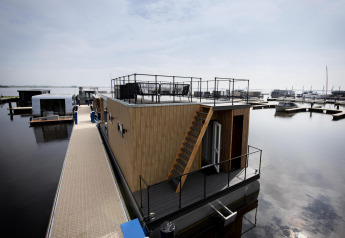 Casa flotante 'Riggelbrug' en Welcome In - Friesland, Países Bajos, con terraza superior y vista al muelle.