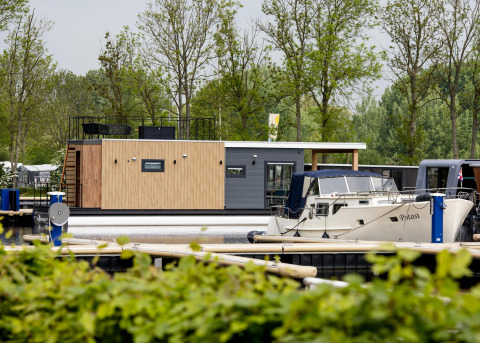 Casa flotante 'Riggelbrug' en Welcome In - Friesland, Países Bajos, atracada junto a una lancha en el muelle.