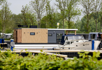 Casa flotante 'Riggelbrug' en Welcome In - Friesland, Países Bajos, atracada junto a una lancha en el muelle.