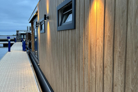 Casa flotante moderna con paneles de madera e iluminación cálida a lo largo del muelle en Friesland, Holanda.