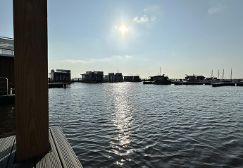 Vista soleada del agua y casas flotantes en Houseboat 'Riggelbrug', Welcome In - Friesland, Países Bajos.