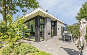 Moderne Natuurlodge ved Recreatiepark het Esmeer i Holland med store vinduer og flisebelagt terrasse.