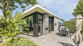 Moderna Natuurlodge al Recreatiepark het Esmeer nei Paesi Bassi, con ampie vetrate e patio arredato.