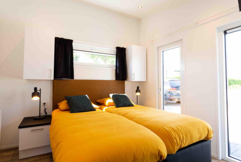 Dormitorio moderno con dos camas individuales, edredones amarillos y luz natural en Natuurlodge, Recreatiepark het Esmeer.