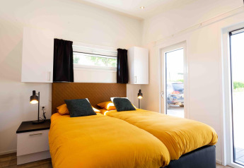 Bright bedroom with twin beds, yellow duvets, natural light in Natuurlodge at Recreatiepark het Esmeer, Netherlands.