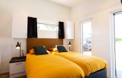Moderne slaapkamer met twee aparte bedden en gele dekbedden in Natuurlodge, Recreatiepark het Esmeer.
