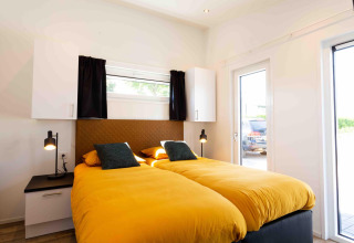 Dormitorio moderno con dos camas individuales, edredones amarillos y luz natural en Natuurlodge, Recreatiepark het Esmeer.