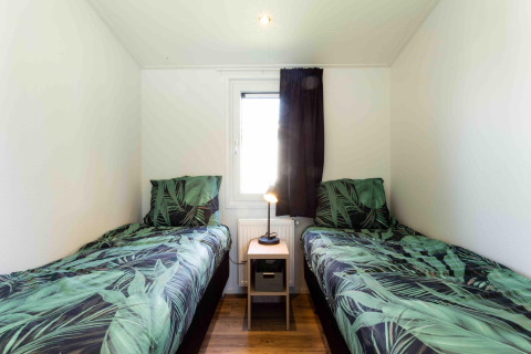Dos camas individuales con ropa de cama de hojas verdes en Natuurlodge, Recreatiepark het Esmeer, Países Bajos.