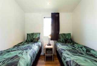 Zwei Einzelbetten mit grüner Blattbettwäsche in einem Zimmer der Natuurlodge, Recreatiepark het Esmeer.