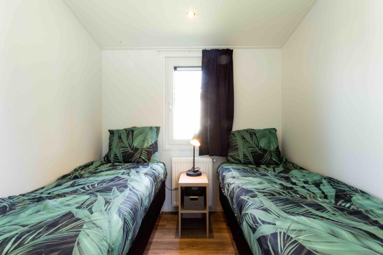 Twin beds with leafy green bedding in a bright room at Natuurlodge, Recreatiepark het Esmeer, Netherlands.