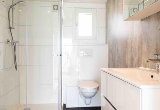 Moderne badkamer van Natuurlodge op Recreatiepark het Esmeer in Nederland, met douche en hangtoilet.