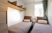 Bright, minimal twin bedroom in Cosy Unique lodge at Maasduinen, Netherlands, with shelves and a window.