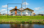 Lodge moderne Anker à Tusken de Marren aux Pays-Bas, grandes baies vitrées et jardin vert près de l’eau.