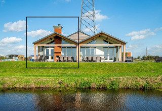 Moderne lodge Anker bij Tusken de Marren in Nederland met grote ramen en zicht op het gras en water.