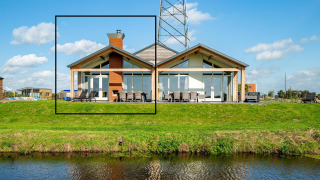 Moderne lodge Anker bij Tusken de Marren in Nederland met grote ramen en uitzicht op grasveld aan water.