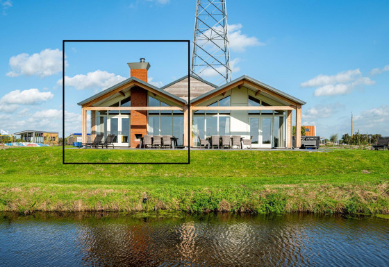 Modern lodge Anker at Tusken de Marren in the Netherlands with large windows and a grassy waterfront view.