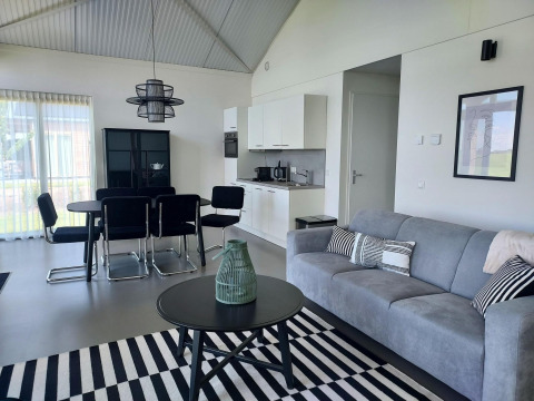 Salon moderne d’un lodge à Anker, Tusken de Marren, Pays-Bas, avec canapé gris, salle à manger et kitchenette.