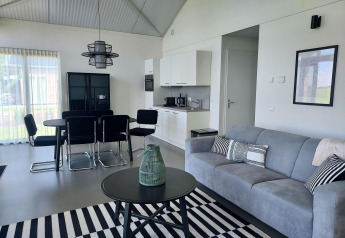 Moderne lodge-living bij Anker, Tusken de Marren, Nederland, met grijze zetel, eetset en keukenhoek.