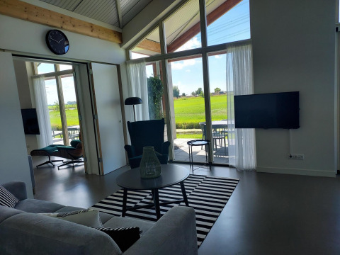 Vista interior de una cabaña moderna con muebles elegantes y grandes ventanales hacia los campos holandeses.