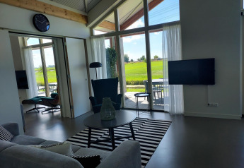 Vista interior de una cabaña moderna con muebles elegantes y grandes ventanales hacia los campos holandeses.