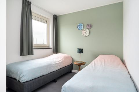 Luminoso dormitorio con dos camas individuales, pared verde y ventana en la casa Anker, Tusken de Marren, Países Bajos.