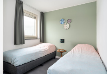 Luminoso dormitorio con dos camas individuales, pared verde y ventana en la casa Anker, Tusken de Marren, Países Bajos.