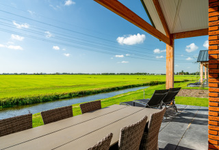View from Anker lodge at Tusken de Marren, Netherlands: patio with table, fields, canal, and sunny sky.