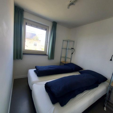 Petite chambre avec deux lits simples et literie bleu marine au lodge Anker, Tusken de Marren, Pays-Bas.