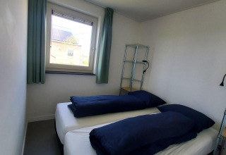 Petite chambre avec deux lits simples et literie bleu marine au lodge Anker, Tusken de Marren, Pays-Bas.