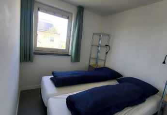 Kleine kamer met twee enkele bedden en donkerblauw beddengoed in Anker lodge, Tusken de Marren, Nederland.