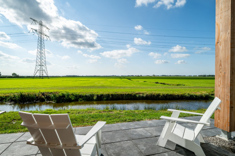 Deux chaises blanches en terrasse face aux champs verts et lignes électriques à la lodge Anker aux Pays-Bas.