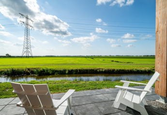Twee witte stoelen op een terras met zicht op groene velden en hoogspanningsmast bij Anker, Nederland.