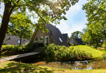 Casa pequeña Wellness Lodge en Hof van Salland, Países Bajos, rodeada de vegetación y un estanque.