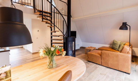 Moderne interiør i Wellness Lodge, Hof van Salland, med lædersofa, spiraltrappe og friske blomster.