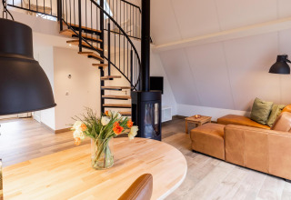 Interno accogliente di Wellness Lodge a Hof van Salland, Paesi Bassi, con divano in pelle e scala a chiocciola.