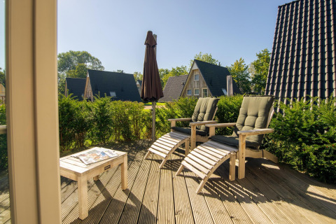 Terrazza soleggiata in legno con sdraio e tavolo al Wellness Lodge, Hof van Salland, Paesi Bassi, immersa nel verde.