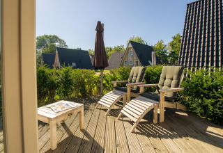 Terrazza soleggiata in legno con sdraio e tavolo al Wellness Lodge, Hof van Salland, Paesi Bassi, immersa nel verde.