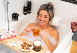 Mujer relajándose en una bañera con té, chocolates y velas en Wellness Lodge, Hof van Salland, Países Bajos.