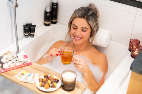 Donna si rilassa nella vasca da bagno con tè, cioccolatini e candele al Wellness Lodge, Hof van Salland, Paesi Bassi.