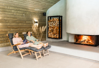 Dos personas relajándose en Wellness Lodge con chimenea y leña en Hof van Salland, Países Bajos.