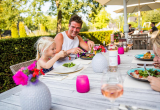 Familia disfruta de una comida al aire libre con vino y ensalada en Wellness Lodge en Hof van Salland.