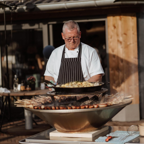 En kok tilbereder mad udendørs på grill ved Wellness Lodge, Hof van Salland, Holland, i solskin.