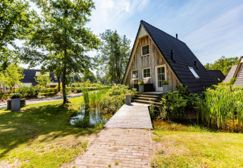 Tiny Wellness Lodge au Hof van Salland, Pays-Bas, avec façade bois, étang et passerelle bordée de verdure.