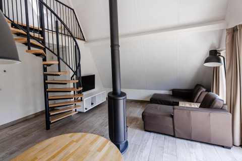 Moderne stue i tiny house Wellness Lodge, Hof van Salland, Holland, med spiraltrappe og lædersofa.