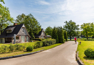 Uomo passeggia con cane vicino a Wellness Lodge, Hof van Salland, Paesi Bassi, tra casette e natura.