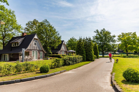 Uomo passeggia con cane vicino a Wellness Lodge, Hof van Salland, Paesi Bassi, tra casette e natura.