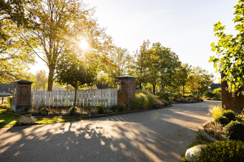 Indgang til Wellness Lodge ved Hof van Salland i Holland, omgivet af grønne træer og sollys i baggrunden.